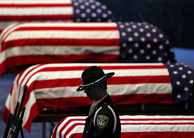 An Oakland Police honor guard stands his post next to the flag-draped caskets of Oakland Police Officers Oakland Police Officers Sgt. Mark Dunakin, 40, John Hege, 41, Sgt. Ervin Romans, 43, and Sgt. Daniel Sakai, 35, in Oracle Arena on Friday, Mar. 27, 2009, in Oakland, Calif. Thousands of mourners have gathered with the families of four slain Oakland police officers for a joint funeral that drew law enforcement from around the world. (AP Photo/Michael Macor, Pool)