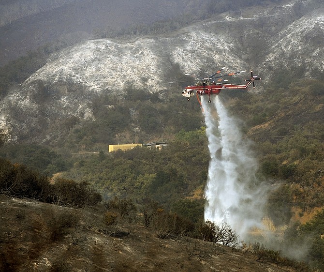 A firefighting helicopter drops water on a hot spot near Santa Barbara, Calif., Friday, May 8, 2009. A wildfire raging along mountain slopes burned more houses Friday as it expanded along a five-mile front above normally serene coastal communities where more than 30,000 people have been forced from their homes (AP Photo/Chris Carlson)