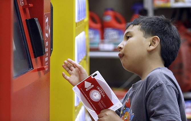 ** FOR USE SUNDAY, JUNE 21 AND THEREAFTER ** In this photo made Tuesday, June 9, 2009, Sydney Ragpala, 7, waits for a DVD to pop out of a Redbox rental unit in a north Seattle grocery store.  Redbox, which is now owned by Coinstar Inc., puts its bright red kiosks in places like supermarkets and Wal-Marts, stocks them with new releases and charges $1 per day. At that price, it&#039;s no wonder budget-friendly Netflix is worried--its cheapest plan runs $5 for two movies a month, or $2.50 each. (AP Photo/Elaine Thompson)