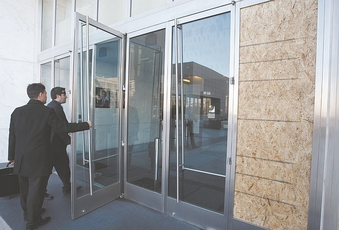 Two people enter a federal building in Las Vegas with a board that covers a broken window, Tuesday, Jan. 5, 2010. A gunman opened fire in the lobby of a federal building in downtown Las Vegas on Monday, killing one court officer and wounding a second before he was shot to death. (AP Photo/Paul Sakuma)