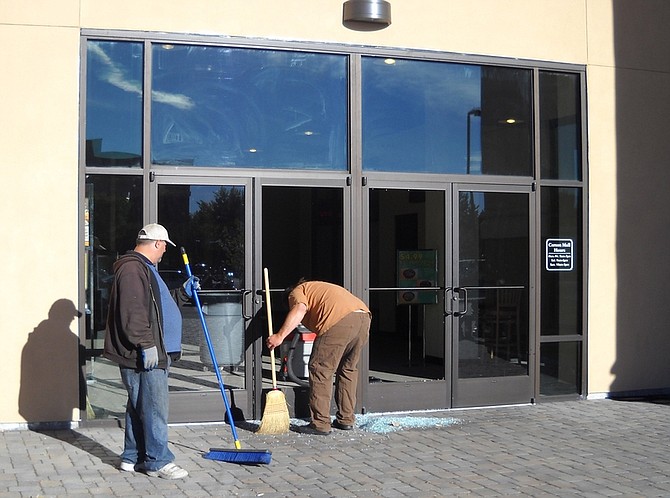 Carson Mall maintenance workers clean up shattered glass this mornng on two doors on the east side of the building after an unknown person broke into the mall, then broke into two businesses inside.