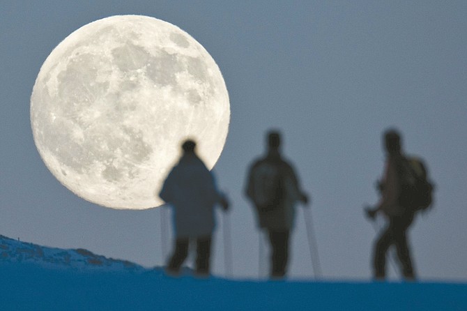 In this photo made available on Tuesday, Dec. 21, 2010, three snowshoe hikers watch the almost full moon rising behind the Weissfluhjoch mountain in Arosa, Switzerland, on Monday, Dec. 20, 2010. (AP Photo/Keystone, Alessandro Della Bella)