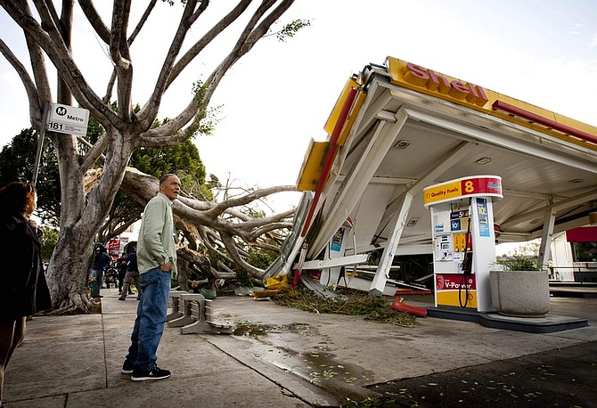 Keith Curo, of Pasadena, stops to look over the damage caused by a fallen tree at a Shell gas station on the corner of North San Gabriel Avenue and East Colorado Boulevard, Thursday, Dec. 1, 2011, in Pasadena, Calif.   Some of the worst winds in years blasted through California overnight, sweeping through canyons, gusting up to 97 mph, and toppling trees and trucks while knocking out power to hundreds of thousands of people.  (AP Photo/Bret Hartman)
