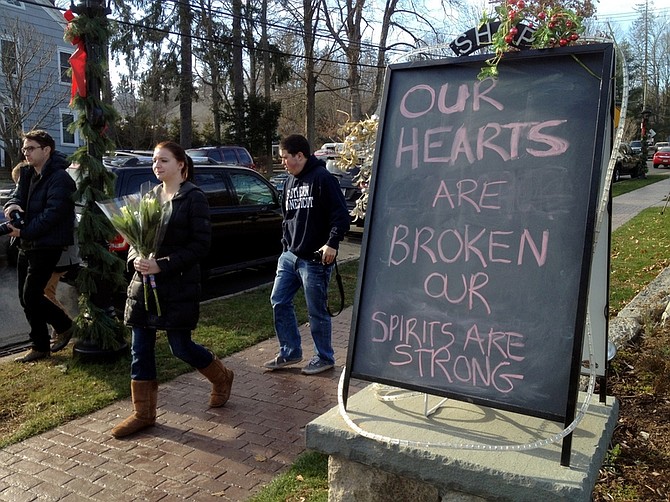 Jessica Henderson, 19, walks past a sign with a bouquet of flowers to lay at a memorial at The Sandy Hook School in Newtown, Conn., on Saturday, Dec. 15, 2012. The massacre of 26 children and adults at Sandy Hook Elementary school elicited horror and soul-searching around the world even as it raised more basic questions about why the gunman, 20-year-old Adam Lanza, would have been driven to such a crime and how he chose his victims. (AP Photo/Allen Breed)