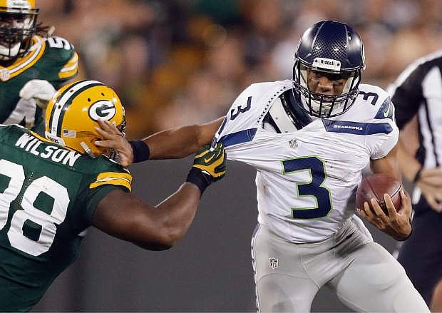 FILE - In this Aug. 23, 2013, file photo,k Seattle Seahawks quarterback Russell Wilson tries to get away from Green Bay Packers&#039; C.J. Wilson during the second half of an NFL preseason football game in Green Bay, Wis. As Super Bowl champions, the Seahawks get to kick off the NFL&#039;s regular season by hosting the Packers on Sept. 4. That Thursday game is the first of four prime-time games on opening weekend. (AP Photo/Jeffrey Phelps, File)