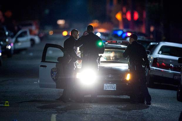 In this Monday Nov. 25, 2013 photo, Oakland police officers confer and gather evidence at the scene of a multiple shooting at the intersection of 96th Avenue and Olive Street in Oakland, Calif. Seven men were wounded, two critically, when gunfire erupted on an Oakland street and continued for several blocks, police said. (AP Photo/Bay Area News Group, D. Ross Cameron)