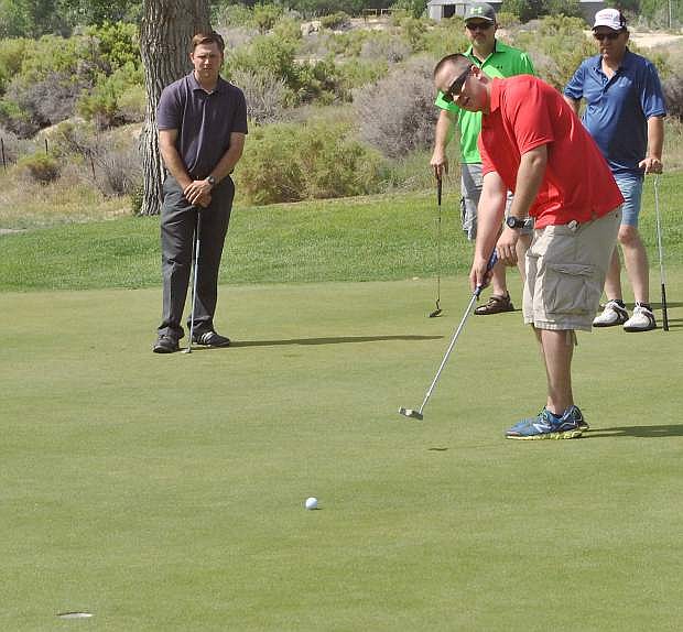 Chris Decker, red, puts on the green while his foursome watches quietly from behind.