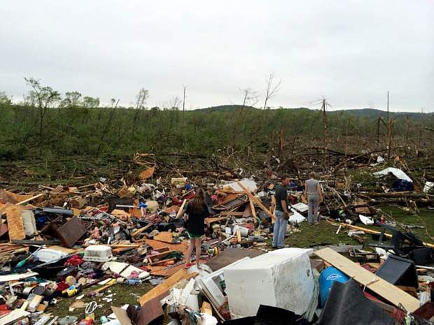 In this Monday, April 28, 2014, photo taken with a cell phone, Emily Tittle, right, Jon Zieske, center, and his daughter Leah, left, look through rubble after a tornado stuck Sunday, in Paron, Ark. Tittle said she, her eight siblings and her parents went for safety under the stairs in the two-story house, but only half of them made it before the walls were obliterated by the twister that left just the foundation behind. Her father, Rob Tittle, and two sisters, Tori, 20, and Rebekah, 14, were killed in the storm. (AP Photo/Christina Huynh)