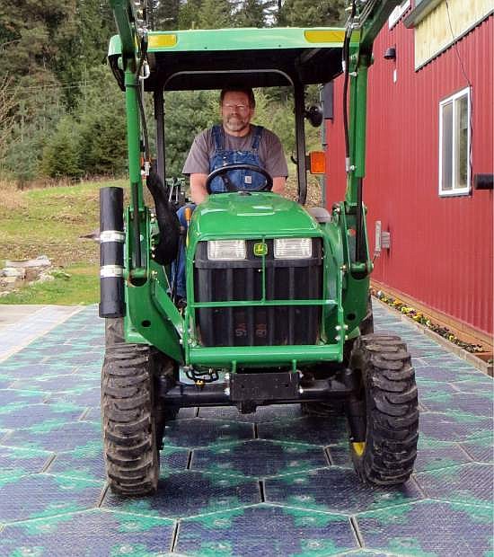 In this May 2014, photo provided by Solar Roadways, Scott Brusaw drives a tractor on a prototype solar-panel parking area at his company&#039;s business in Sandpoint, Idaho. Brusaw&#039;s idea for solar-powered roads has gone viral and raised more than $1.4 million in crowdsourced funding. Brusaw is proposing to pave driveways, parking lots, bike trails and, eventually, highways with hexagon-shaped solar panels that will produce electricity and could even propel electric cars. (AP Photo/Solar Roadways)