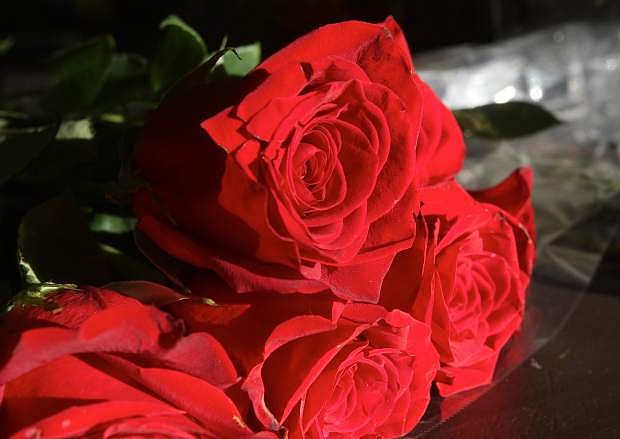 Red roses that will be used in a bouquet sit on the counter at the Flower Bucket floral shop.