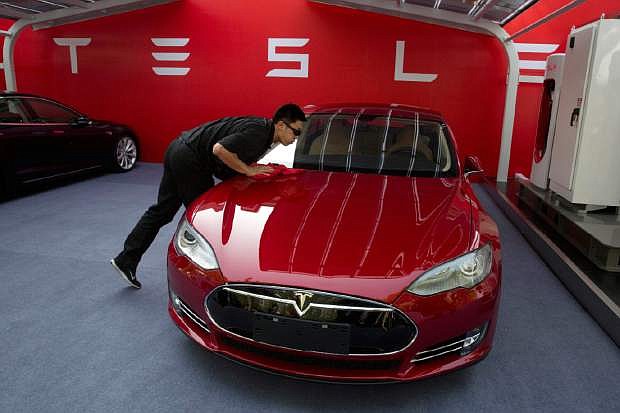 FILE - In this April 22, 2014 file photo, a worker cleans a Tesla Model S sedan before a event to deliver the first set of cars to customers in Beijing. Tesla Motors on Thursday, March 19, 2015 said it is updating its Model S electric car to help ease drivers&#039; worries about running out of battery charge.  (AP Photo/Ng Han Guan, File)