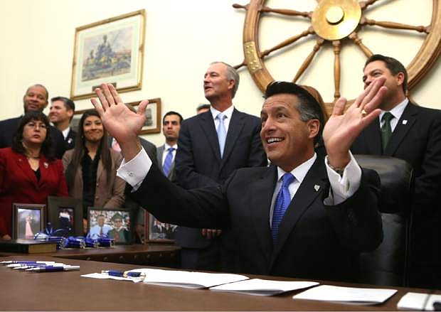 Surrounded by lawmakers and staff members, Nevada Gov. Brian Sandoval signs into law an unprecedented package of incentives to bring Tesla Motors&#039; $5 billion battery factory to the state, at the Capitol, in Carson City, Nev., on Thursday, Sept. 11, 2014. (AP Photo/Cathleen Allison)