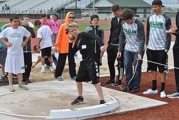 Brady Jack stands ready to throw in the fifth-grade boys shotput event while several members of the Wave boys track and field team supervise the event.