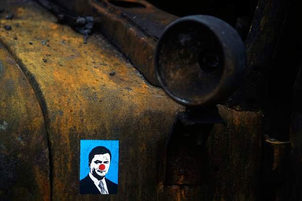 A sticker depicting Ukrainian President Viktor Yanukovych is placed on a burned military truck in Kiev, Ukraine, Sunday, Feb. 23, 2014. The Kiev protest camp at the center of the anti-President Viktor Yanukovych movement filled with more and more dedicated demonstrators Sunday morning setting up new tents after a day that saw a stunning reversal of fortune in a political standoff that has left scores dead and worried the United States, Europe and Russia. (AP Photo/ Marko Drobnjakovic)