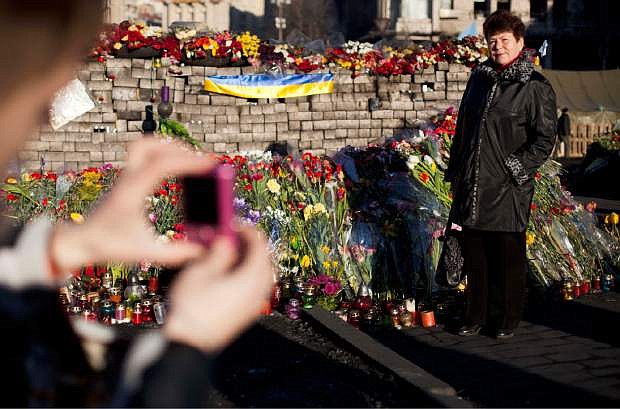 A woman poses for a photograph next to a wall composed of paving stones and adorned with flowers and candles placed in memory of those who died in clashes which took place in late February in Kiev&#039;s Independence Square, Ukraine, Tuesday, March 11, 2014. (AP Photo/David Azia)