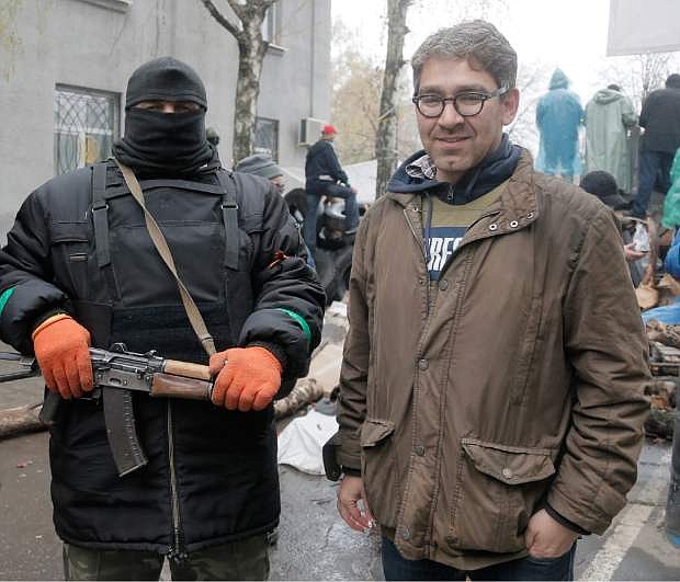 In this photo taken on Sunday, April 13, 2014, a U.S. reporter Simon Ostrovsky, right, stands with a Pro-Russian gunman at seized police station in the eastern Ukraine town of Slovyansk. Pro-Russian gunmen in eastern Ukraine admitted on Wednesday April 23, 2014, that they are holding captive American journalist for Vice News Simon Ostrovsky who has not been seen since early Tuesday.   Ostrovsky has been covering the crisis in Ukraine for some weeks and was reporting about groups of masked gunmen seizing government buildings in eastern Ukrainian. (AP Photo/Efrem Lukatsky)
