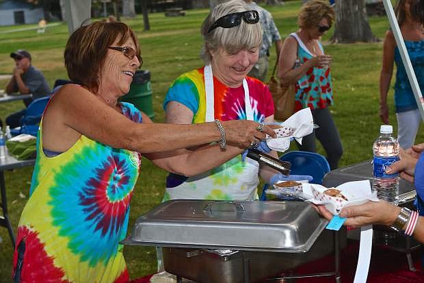 Kris Smith and Alice Magdaleno serve bratwurst to wine train participants Friday evening at Mills Park.