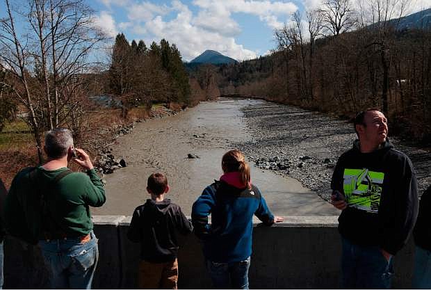 Residents watch as debris comes down the Stillaguamish River from the Whitman Road bridge east of Oso Sunday, March 23, 2014. (AP Photo /The Herald, Mark Mulligan)