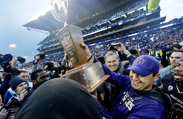 Washington head coach Steve Sarkisian, right, lifts the Apple Cup trophy after being given it by Gov. Jay Inslee, center, after the team beat Washington State in an NCAA college football game Friday, Nov. 29, 2013, in Seattle. Washington won the annual Apple Cup, 27-17. (AP Photo/Elaine Thompson)