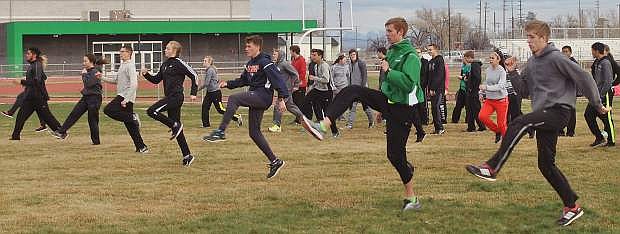 Tristen Thomson, green jacket, leads the Greenwave boys and girls track team in high-knees during practice.