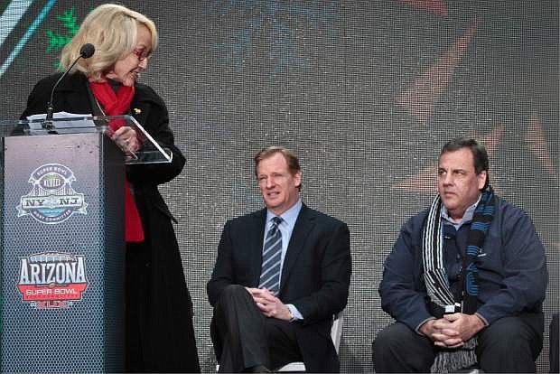 NFL Commissioner Roger Goodell, center, and New Jersey Gov. Chris Christie, right, display different reactions as Arizona Gov. Jan Brewer, left,  speaks during a ceremony to pass official hosting duties of next year&#039;s Super Bowl to Arizona, Saturday Feb. 1, 2014 in New York.   (AP Photo/Bebeto Matthews)