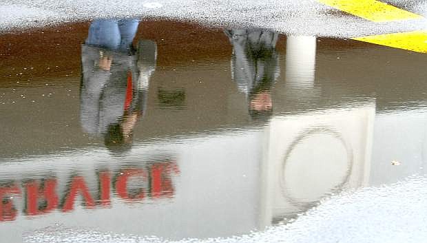 Shoppers leaving the Carson Mall are reflected in a small puddle in the parking lot on Tuesday.