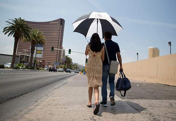 Under the shade of an umbrella with temperatures already in triple digits by mid morning, tourists walk north along Las Vegas Boulevard toward The Strip, Sunday, June 30, 2013 in Las Vegas. Temperatures were on the rise again after the city reported a record overnight low of 89 degrees Sunday and forecasters predicting a high of 116.  (AP Photo/Julie Jacobson)