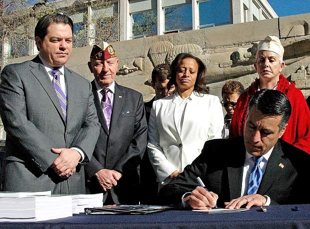 Gov. Brian Sandoval signs Assembly Bill 76 into law Thursday during the annual Veterans and Military Day at the Legislature here at the Nevada Capitol. The law extends the length of time a Veteran with an honorable discharge can receive a tuition waiver from a Nevada state higher-education school from two to five years.