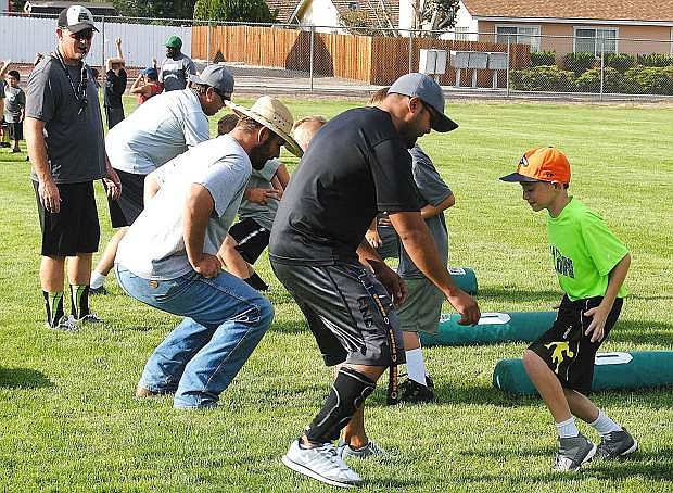 Youth football coaches go over the fundamentals of tackling with players during a camp last week at Churchill County High School.