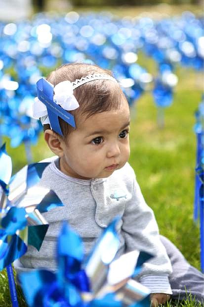 7-month-old Ellie Rose Delgado sits amongst the hundreds of blue pinwheels placed in the Legislative Building&#039;s lawn Friday in observance of Chid Abuse Prevention Month.
