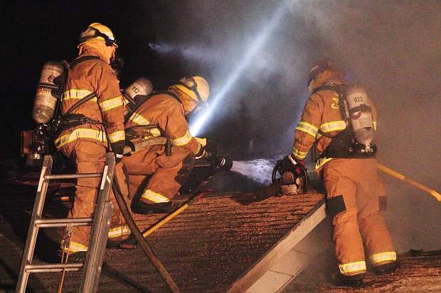 Three firefighters try to knock down the flames on the roof at 3690 Shawnee Saturday night.