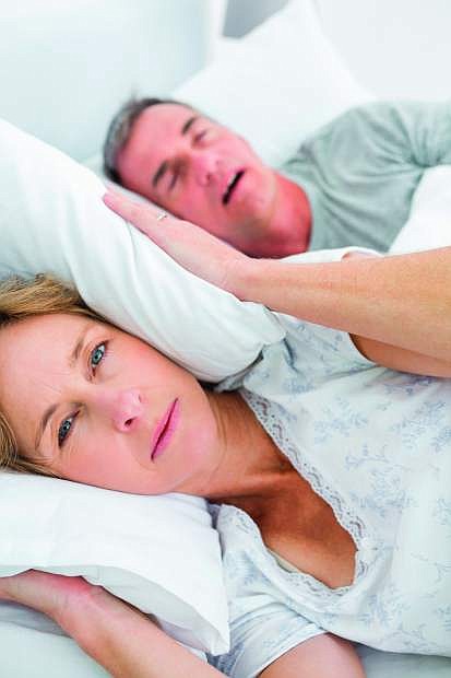 A tired wife blocks her ears from the  noise of her husband&#039;s snoring.