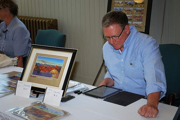 Artist Ron Spears arranges a display of his artwork at the re-dedication of  Nevada&#039;s sesquicentennial postage stamp.