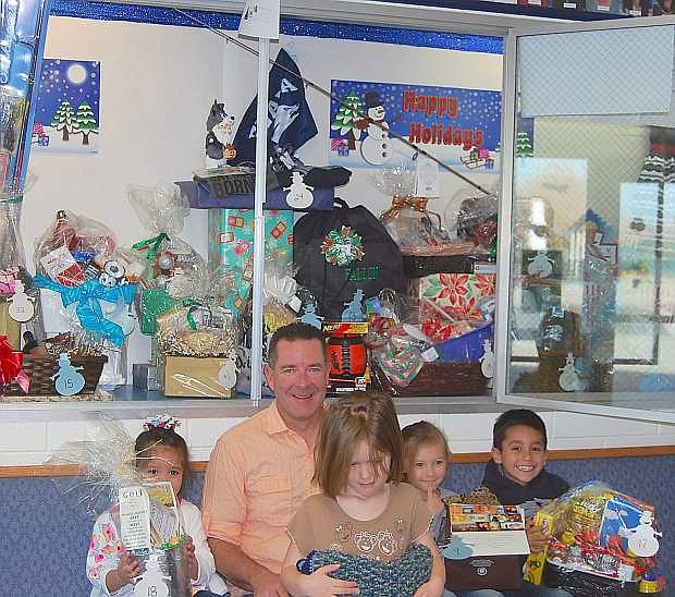 NELC Principal Gregg Malkovich sits in front of a display case with students from left Elizabeth Madera, Sophie Bake, Danielle Fenton and Arad Duenas with gift baskets that will be auctioned off at the Winter Wonderland.