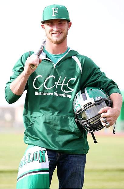 Workman holds Wave baseball bat and Wave football helmet on the turf.