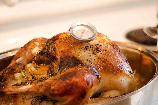 thanksgiving traditional holiday food. Golden color cooked turkey with the thermometer in the metal bowl. its covered with small pieces of rosemary spices. light is coming from the right site of the picture. Big leg of the turkey closed to the camera.