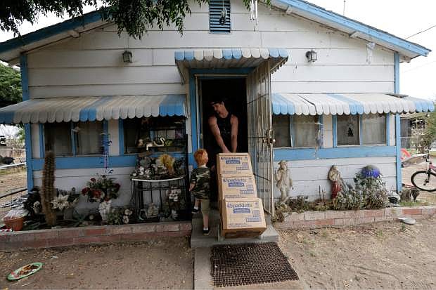 In this July 2, 2015 photo, Billy Dunlap, 21, hauls in boxes of bottled water as his son, Brandon, 3, walks alongside at their home in the community of Okieville on the outskirts of Tulare, Calif. Four generations of Dunlaps share the white house with blue trim Christine Dunlap&#039;s father-in-law built in the 1940s, and little changed in all those years, until her 170-foot well ran dry in February. (AP Photo/Gregory Bull)