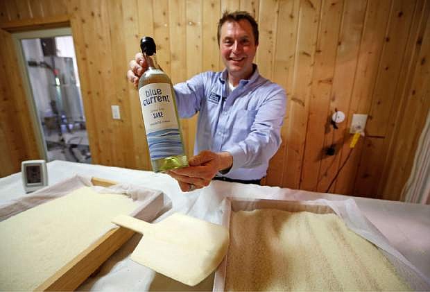 In this photo taken, Friday, June 12, 2015, Dan Ford, founder of the Blue Current Brewery, poses with a bottle of sake at the brewery in Kittery, Maine. Steamed rice is inoculated in a sauna-like koji room for two days as part of the six week brewing process to make &quot;rice wine.&quot; (AP Photo/Robert F. Bukaty)
