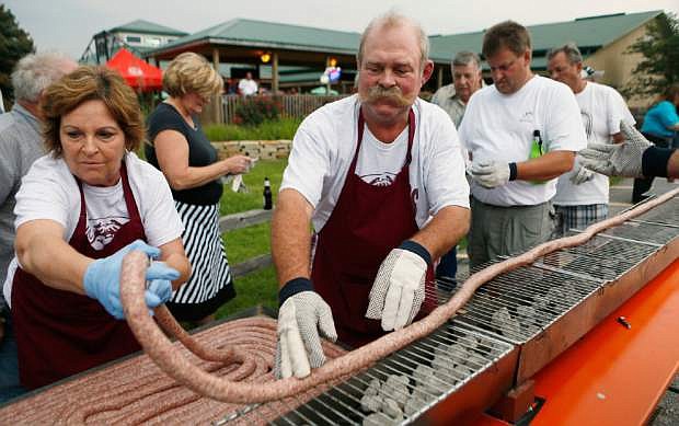 In this Tuesday, Sept. 9, 2014 photo, Mabel and Larry Schubert help lay out a 100 foot-long bratwurst on a grill at the Silver Creek Saloon in Belleville, Ill. About 50 people volunteered to carefully grill the bratwurst without burning or breaking it. The event was a practice run for the Belleville 200th celebration where they will be grilling a 200 foot-long bratwurst on Sept. 21. (AP Photo/Belleville News-Democrat, Zia Nizami)