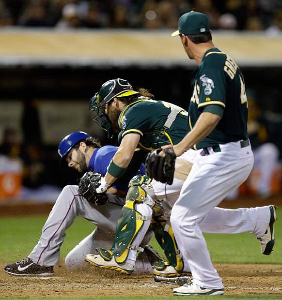 Texas Rangers&#039; Mitch Moreland, left, is tagged out at home plate by Oakland Athletics catcher Derek Norris as pitcher Luke Gregerson, right, backs up the play in the ninth inning of a baseball game Tuesday, April 22, 2014, in Oakland, Calif. (AP Photo/Ben Margot)
