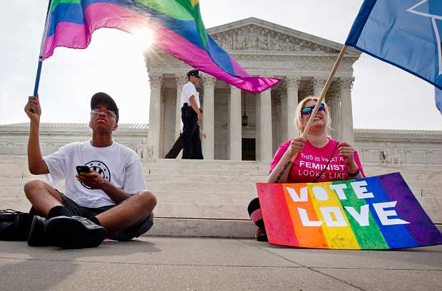 Carlos McKnight, 17, of Washington, left, and Katherine Nicole Struck, 25, of Frederick, Md., hold flags in support of gay marriage as security walks behind outside of the Supreme Court in Washington, Friday June 26, 2015. A major opinion on gay marriage is among the remaining to be released before the term ends at the end of June.  (AP Photo/Jacquelyn Martin)