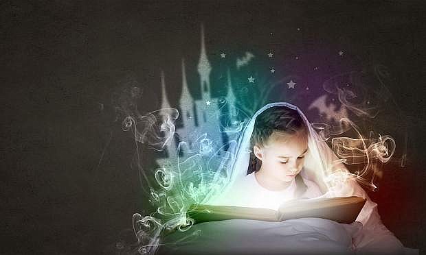 Little cute girl with in bed reading book under blanket