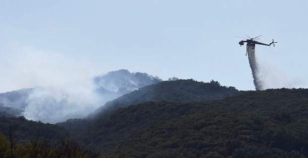 In this photo provided by the Santa Barbara County Fire Department, a Skycrane makes a water drop on hot spots near Hot Spring Canyon and Highway 154 in the Whittier fire area near Santa Barbara, Calif., Wednesday, July 12, 2017. In Southern California, thousands of people remained out of their homes as a pair of fires raged at different ends of Santa Barbara County. The fires broke out amid a blistering weekend heat wave that toppled temperature records. (Mike Eliason/Santa Barbara County Fire Department via AP)