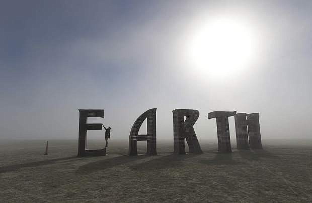 FILE - In this Saturday Aug. 27, 2016, file photo, Anita Vranckx, of Belgium, hangs from the E of an Earth sculpture at Burning Man on a dusty morning on the playa in the Black Rock Desert near Gerlach, Nev. Tens of thousands have braved massive traffic jams to get to the remote stretch of Nevada desert for the 2017 Burning Man festival that runs until Sept. 4, 2017. (Andy Barron/The Reno Gazette-Journal via AP, File)