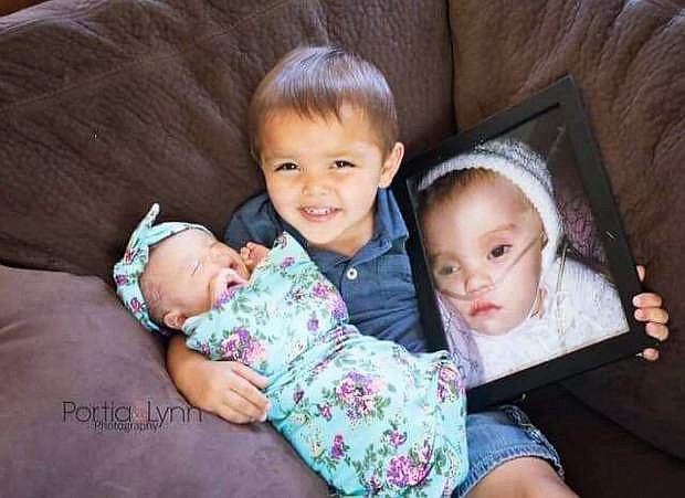Anakin Garcia holds both of his sister:, Wren, left, whom is battling Vanishing White Matter, and a photo of Winter, right, whom died from VHM at 8 months old.