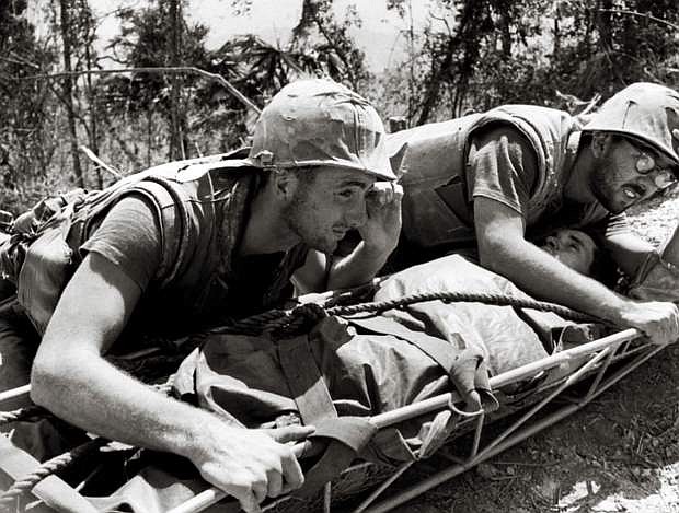 In this photo from the Vietnam War, two Navy corpsmen attend to a wounded Marine waiting for a helicopter just like Medal of Honor winner Don Ballard did 50 years ago.
