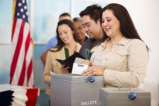 Multi-ethnic group of people stand in line to cast their ballot in the November USA elections at a local polling station. Hispanic woman foreground. Other voters in line background. Ballot box.