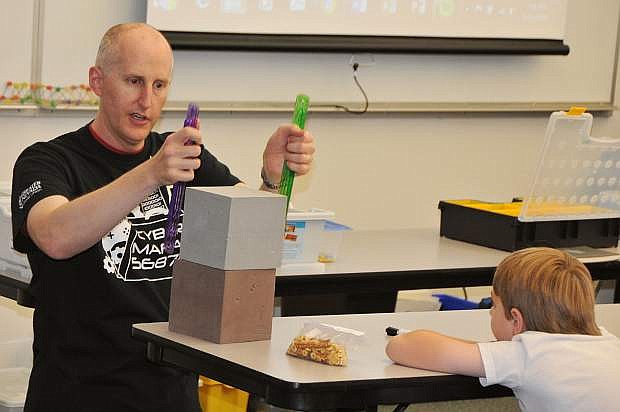 Robotics Camp instructor Scot Duncan leads a lesson explaining why manufacturing tolerances create engineering challenges when trying to pick up two cubes with a single-gripping system as camper Don Winne listens.