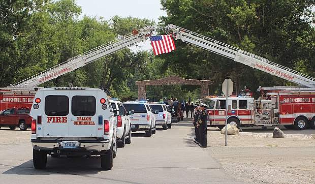 A funeral procession of first responders and private vehicles for fallen firefighter Bert Miller on Friday travels under a flag at the Churchill County Cemetery.