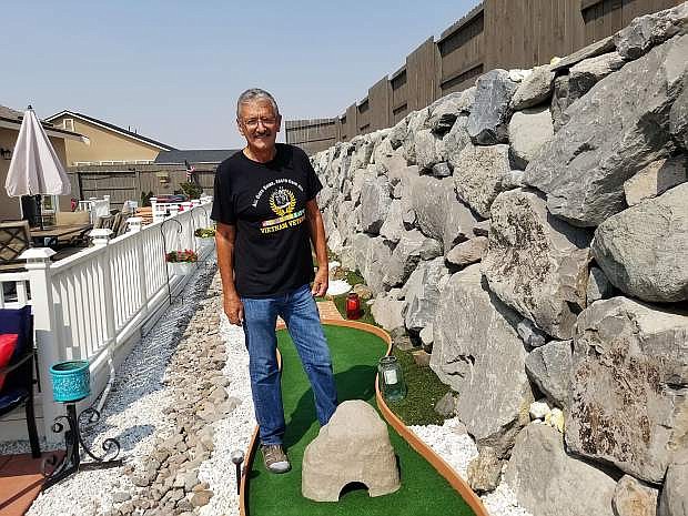 Mike Pulos stands in front of a few holes that make up his 9-hole, backyard miniature golf course.